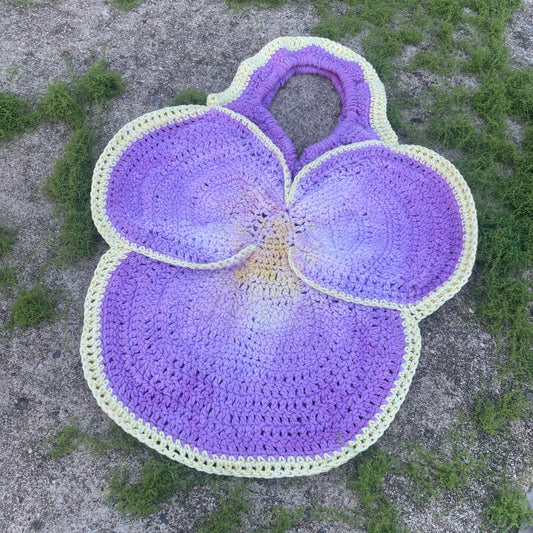 Crocheted purple flower mat with green accents on a textured surface
